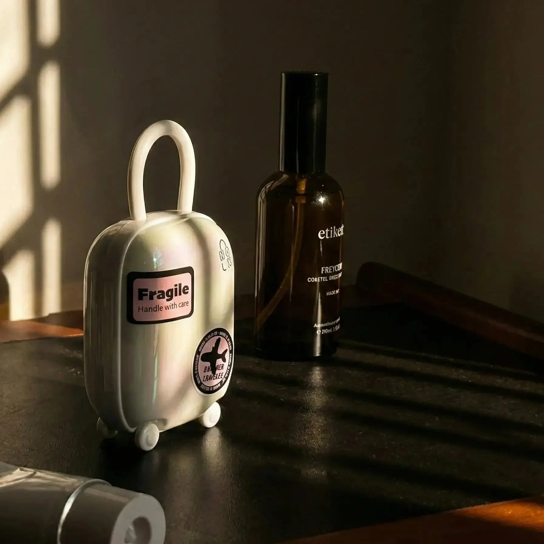 NOX Traveller UV charging case shaped like a miniature suitcase with a Fragile travel label, sitting on a bedside table