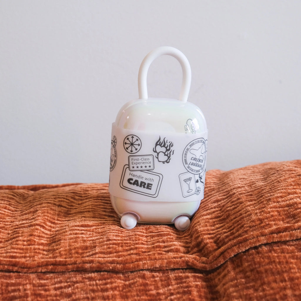 Aesthetic white vibrator case with stickers sitting on an orange pillow