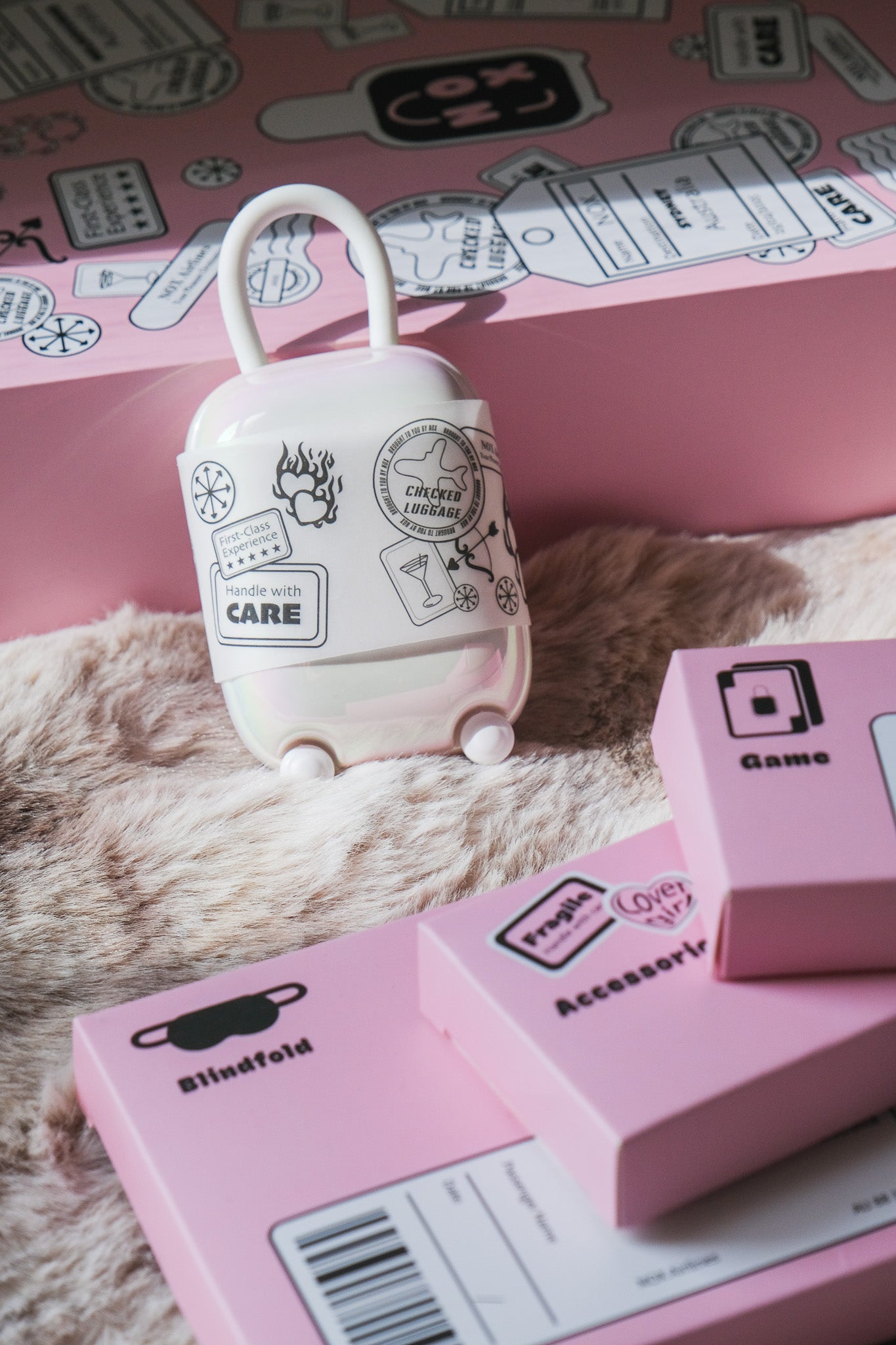 Aesthetic display of the NOX Traveller date night box contents, including the suitcase charger, blindfold, and game boxes on a soft rug.