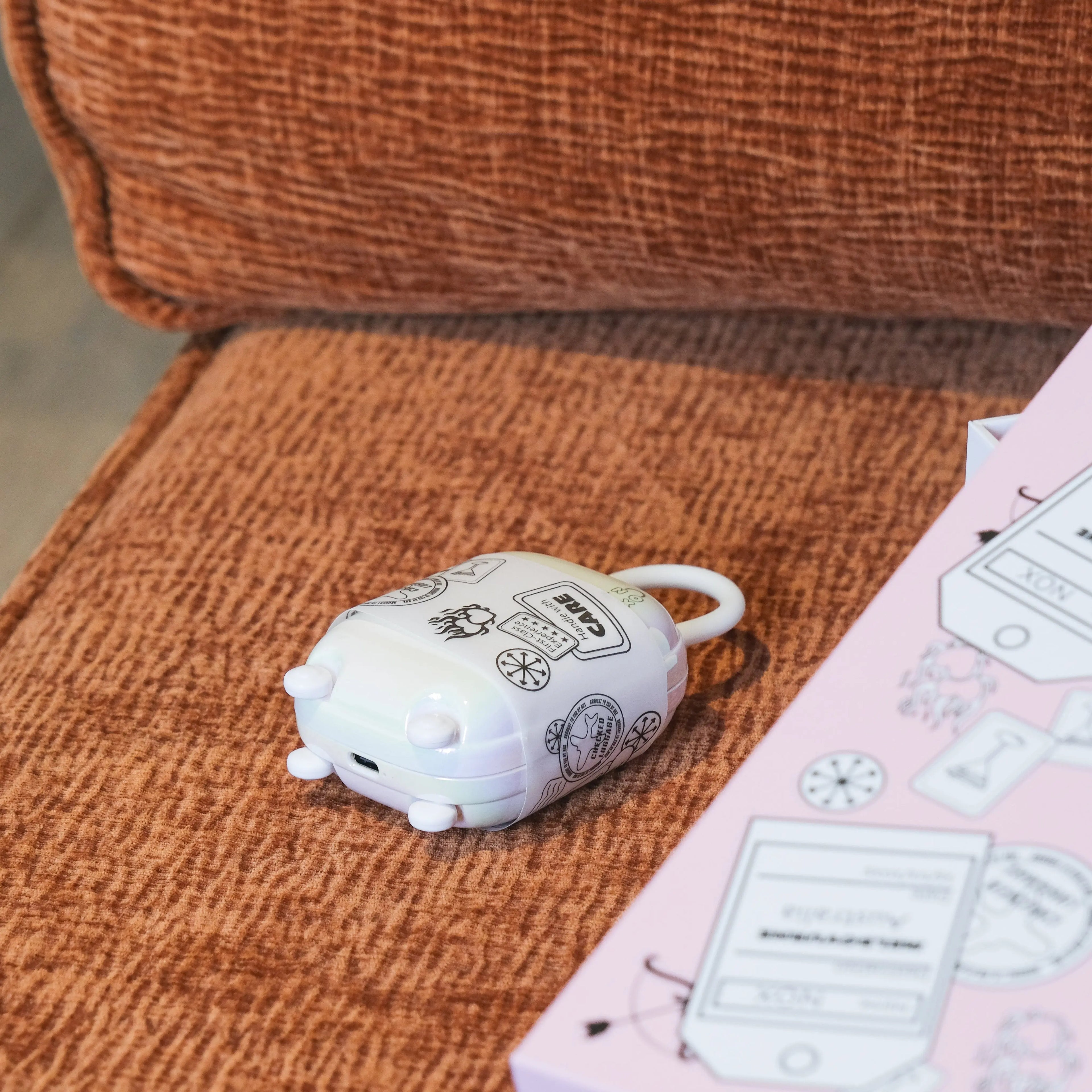 Aesthetic white vibrator case with stickers sitting on an orange pillow