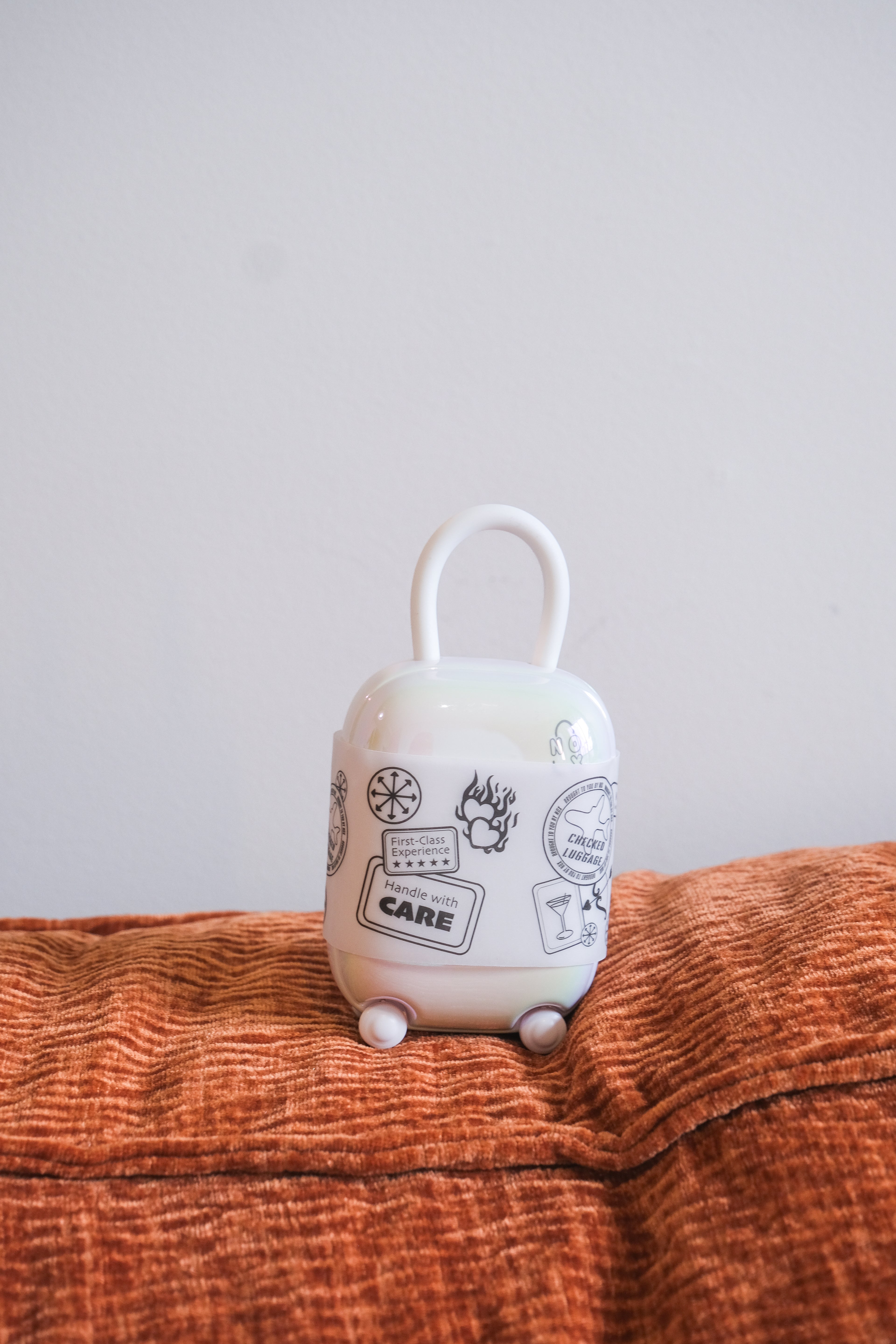 The cute, aesthetic NOX Traveller vibrator charging case with stickers, sitting on a textured orange pillow.