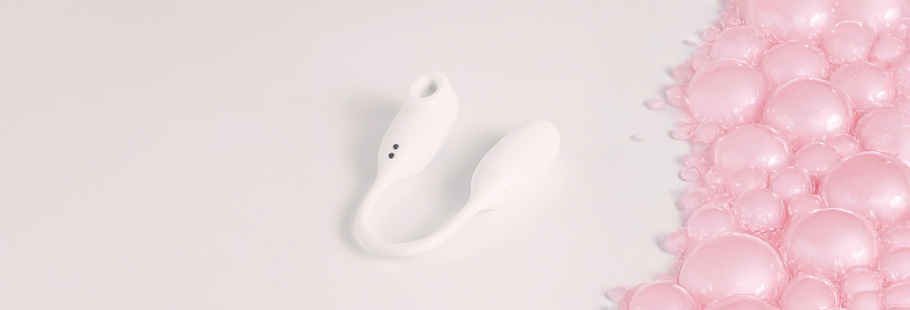 The white NOX Traveller vibrator lying next to pink soap bubbles, showing it is waterproof and bath-friendly.