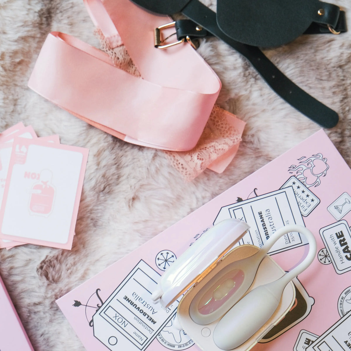 Aesthetic flatlay of the NOX Traveller date-night set: blindfold, card game and the open mini-suitcase case