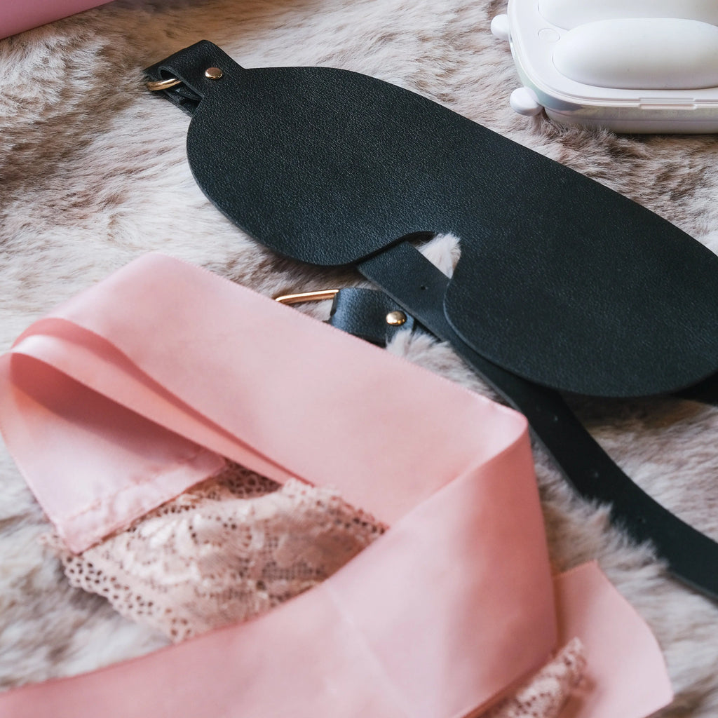 Detail shot of the premium black leather and pink silk blindfolds included in the NOX Traveller kit.