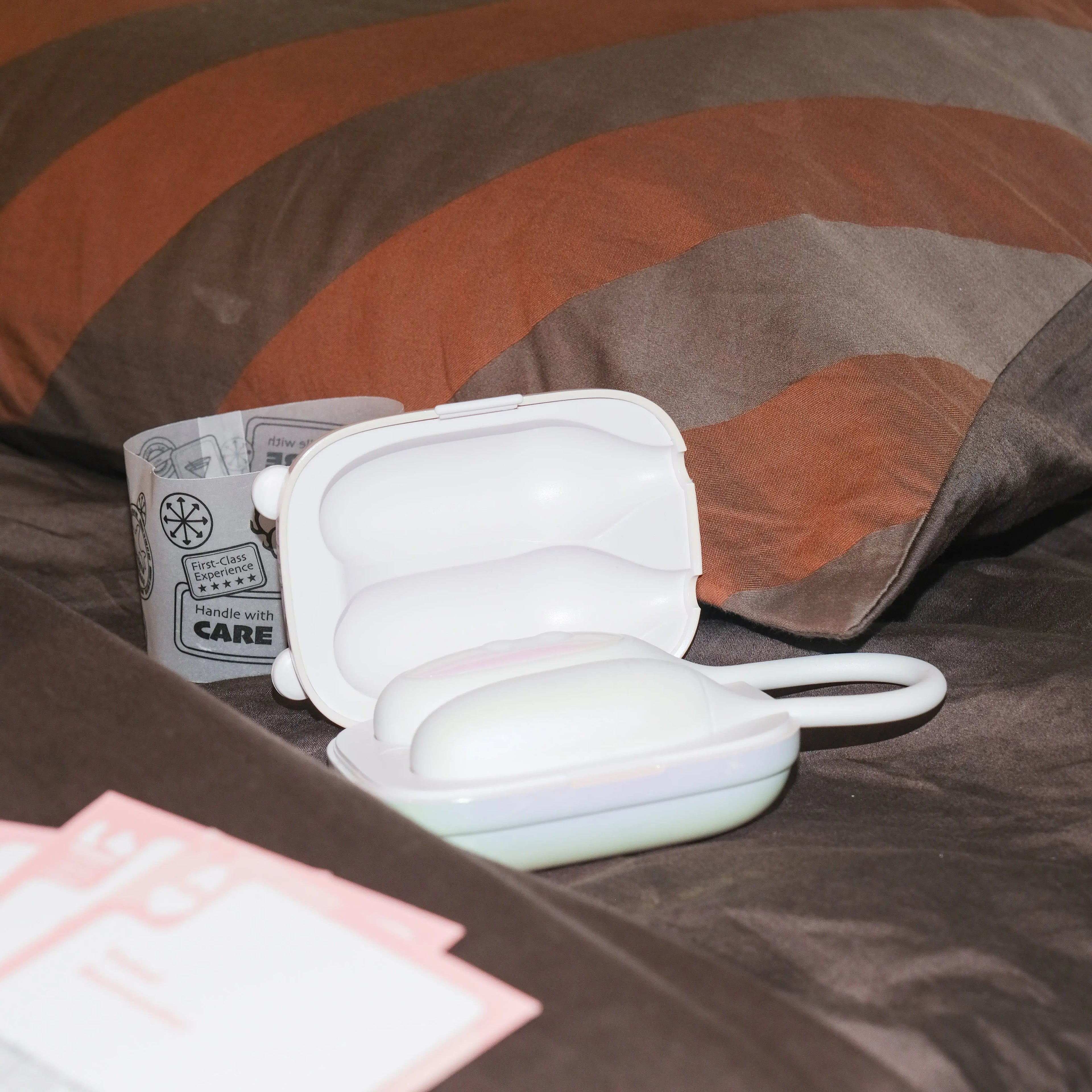 Close-up of the open white NOX Traveller case holding the quiet beginner vibrator, resting on a bed pillow ready for a romantic night in.